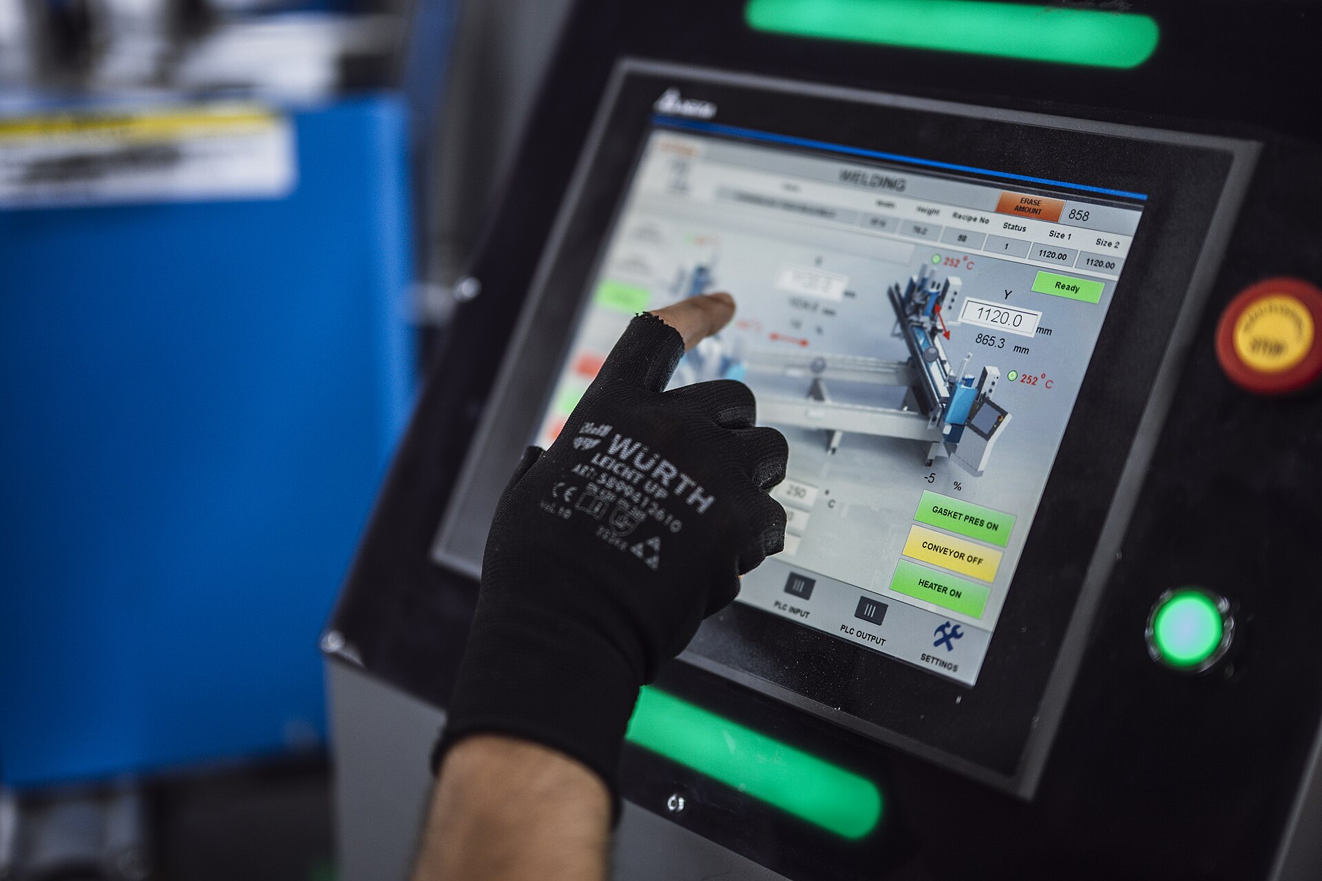 A gloved finger pressing a welding machine's touchscreen controls on the shop floor